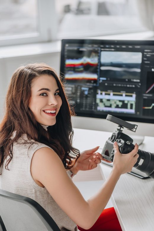 happy art editor holding digital camera near table with computer monitors